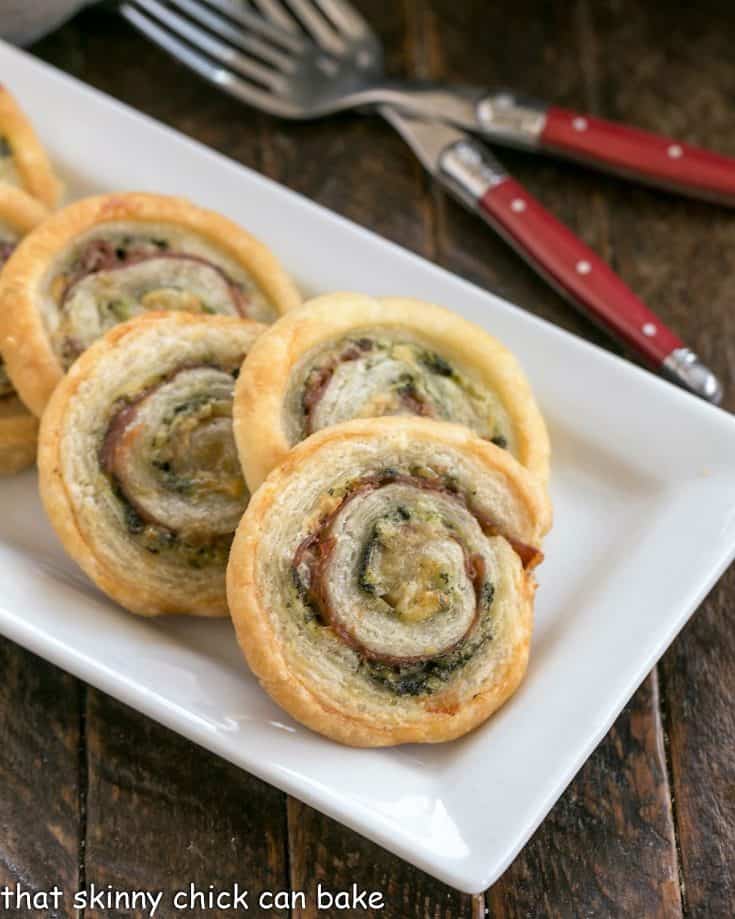 Close view of Prosciutto, Gruyere and Basil Pinwheels on a white ceramic tray with 2 forks