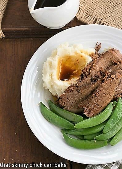 Coffee Glazed Brisket with sugar snap peas and mashed potatoes on a white plate viewed from above.