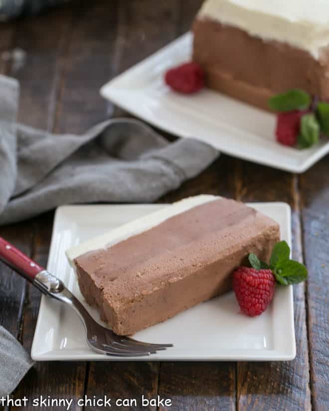 Slice of triple chocolate mousse on a white plate with a red handle fork.