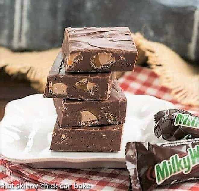 Milky Way Fudge squares stacked on a small white plate with fun-sized Milky Way bars