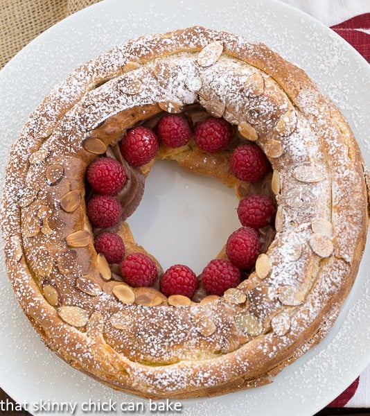 Overhead view of a Paris brest on a white serving plate garnished with raspberries.