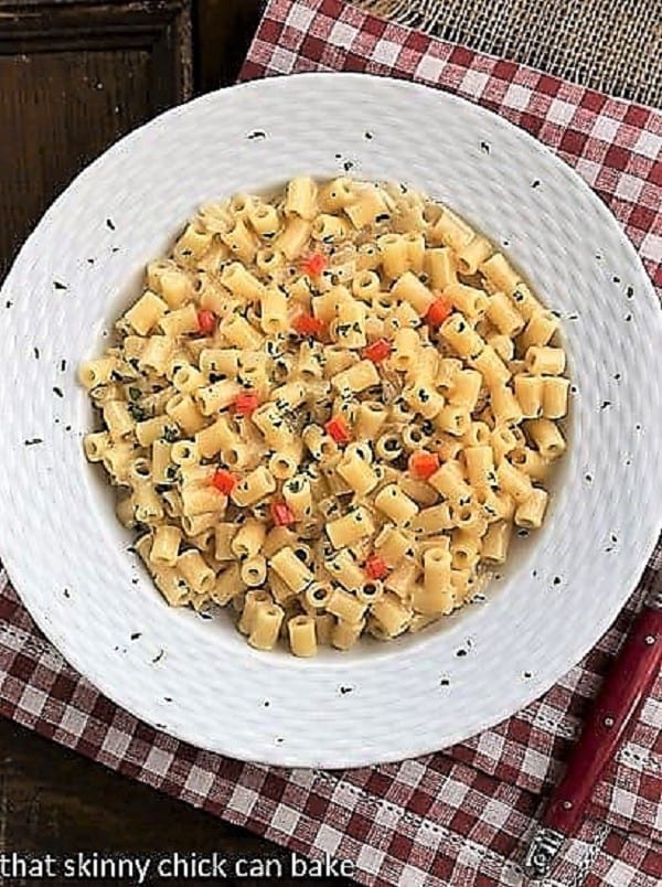 Overhead view of pasta risotto in a white bowl on a red and white checkered napkin