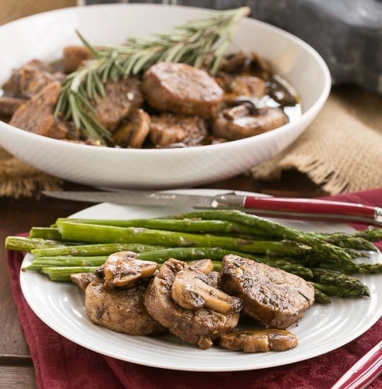 Pork Tenderloin with Maple Balsamic Glaze on a white plate with asparagus spears and a red handle knife