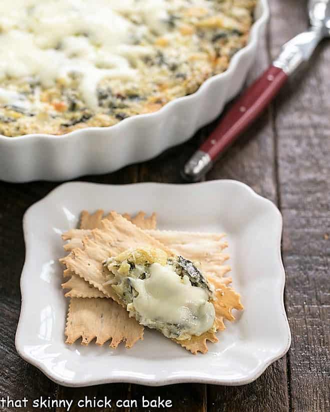 A spoonful of Hot Spinach and Artichoke Dip on an appetizer plate with crackers.