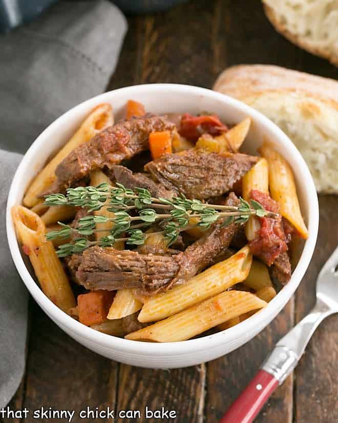 Beef Ragu with penne pasta in a white bowl with bread slice and a fork.