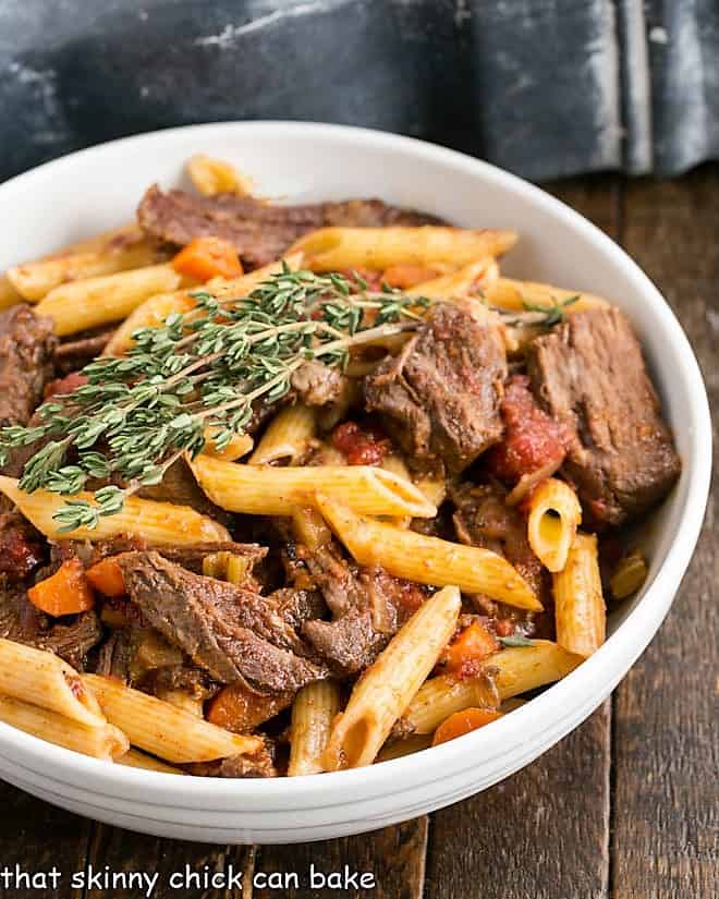 Beef Ragu Pasta in a white serving bowl with a sprig of fresh thyme.
