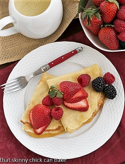 Overhead view of Butter and Rum Crêpes on a white plate with a red handled fork.