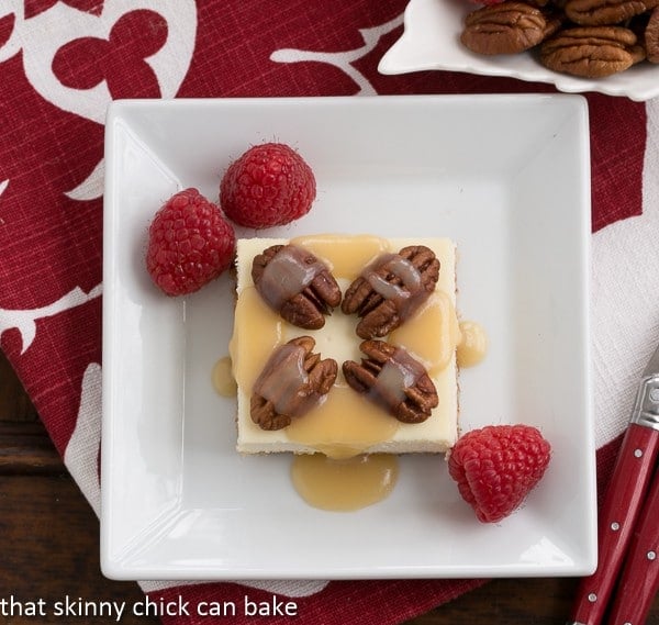 Caramel Pecan Cheesecake Bars on a square white plate on a red and white napkin.