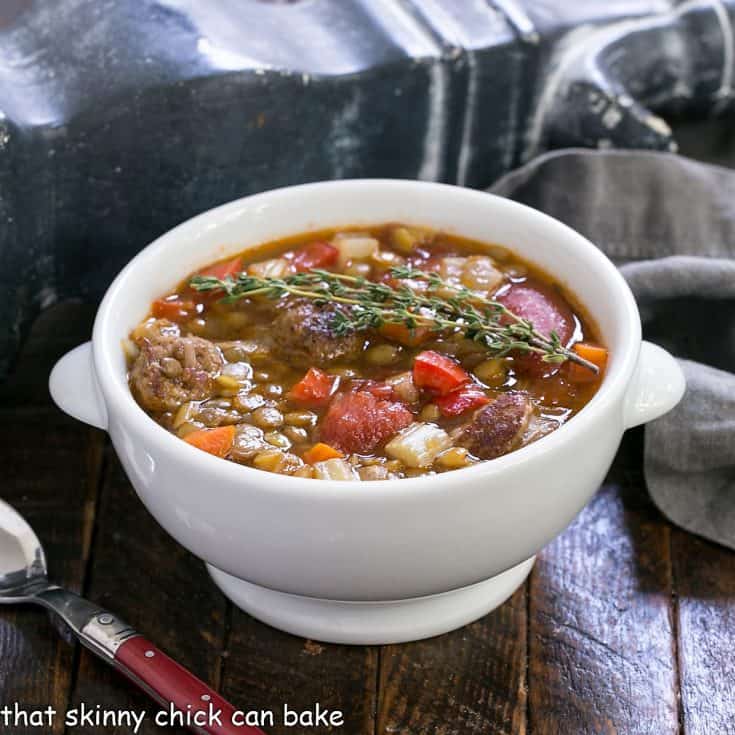 White bowl filled with the best lentil soup, topped with fresh thyme and served with a red handled spoon