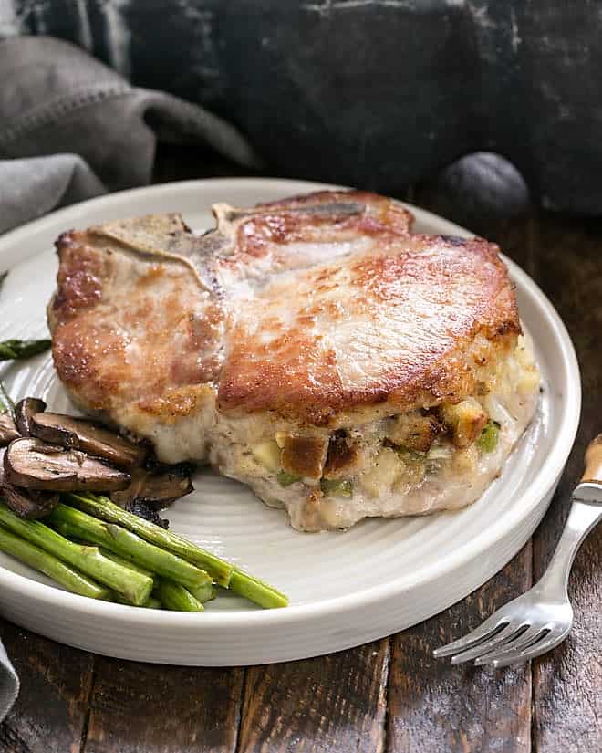 A Stuffed Pork Chop chop on a white dinner plate with asparagus and mushrooms.