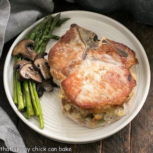 Overhead view of stuffed pork chops on a round white plate with asparagus