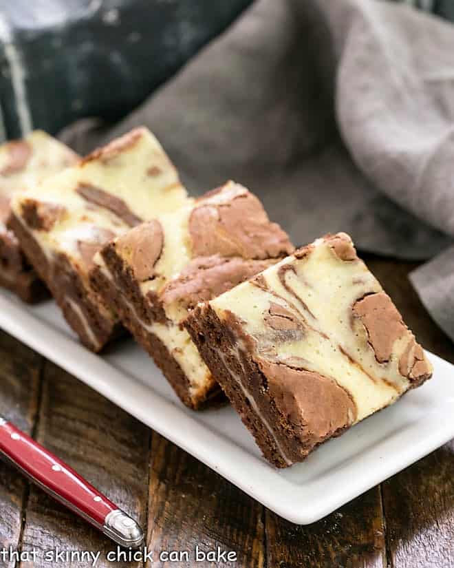 Cheesecake Swirl Brownies lined up on a white ceramic tray with a red handle fork