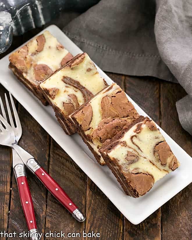 Overhead view of a tray of cheesecake brownies with two red handled forks