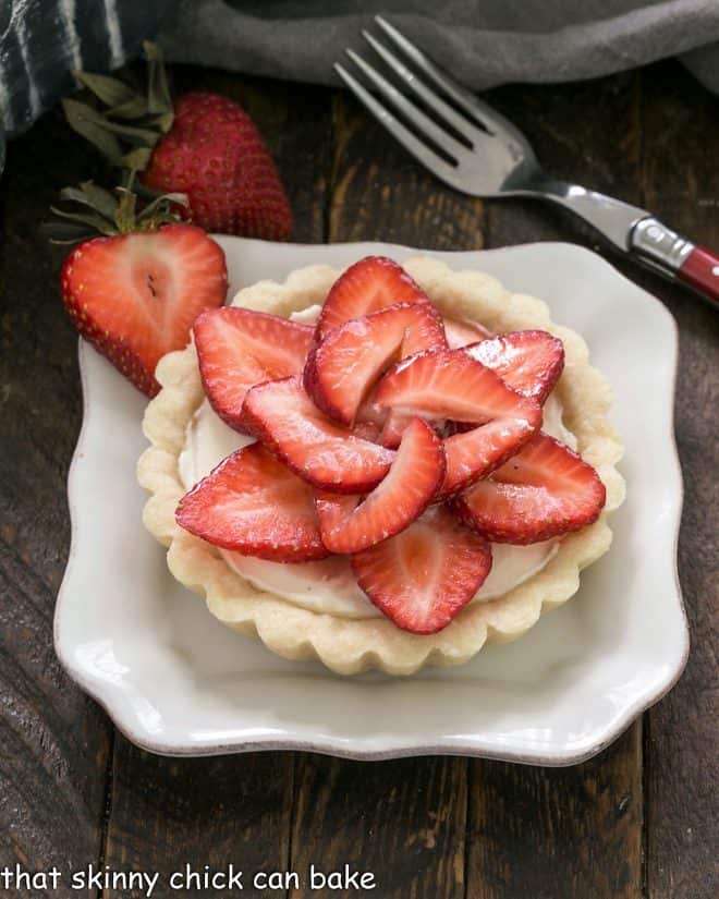 A strawberry tart on a square white plate with a red handled fork