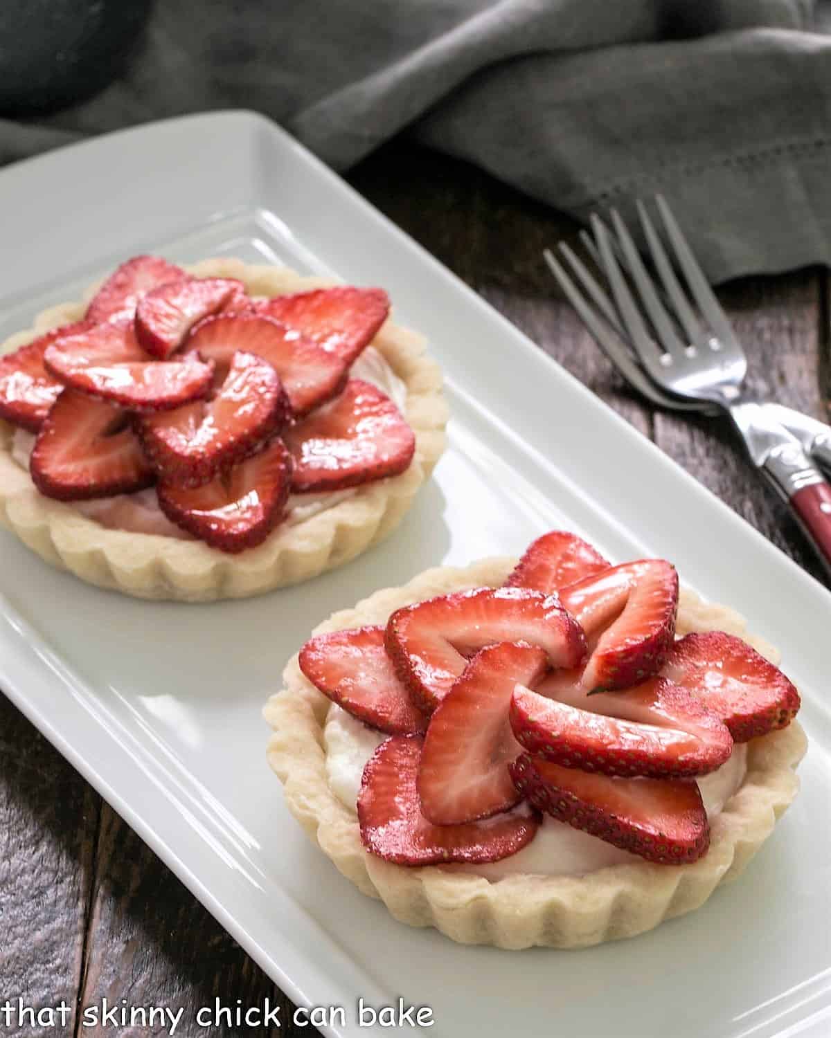 2 fresh strawberry tarts on a white ceramic tray.
