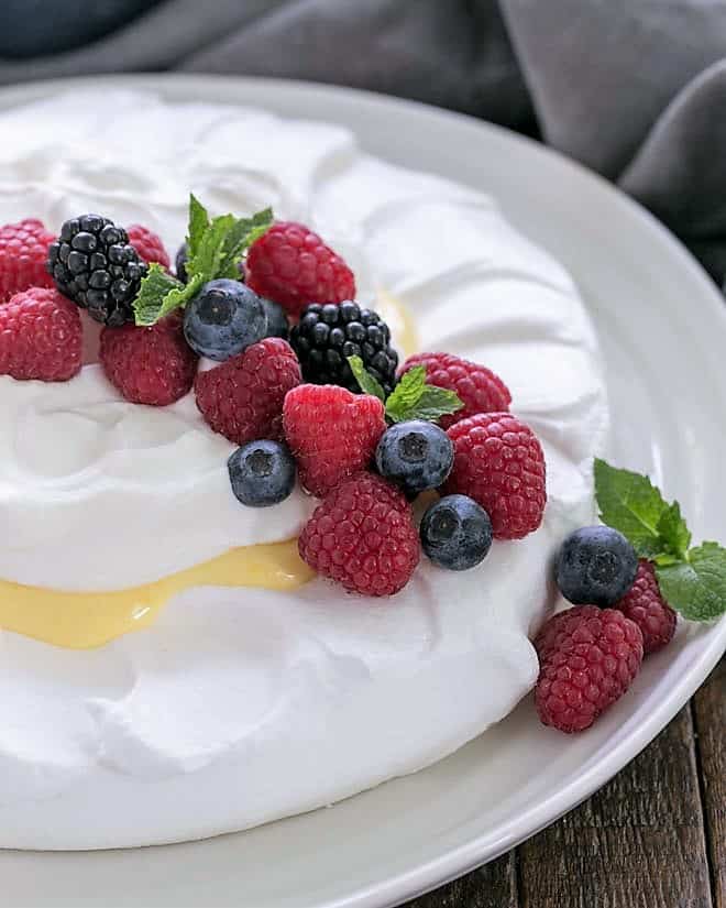 Lemon Pavlova on a white serving plate garnished with berries and mint