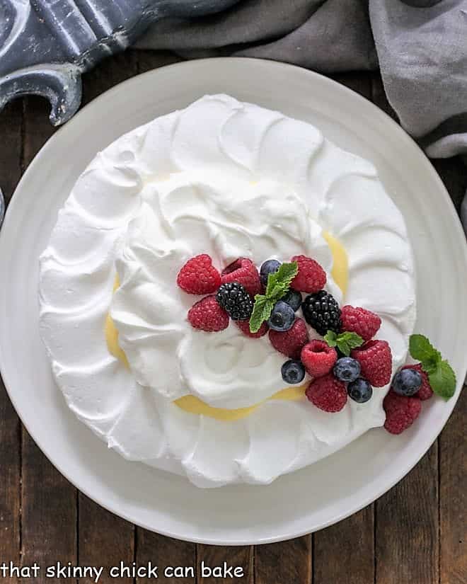 Overhead view of a pavlova dessert topped with lemon cream, whipped cream and berries