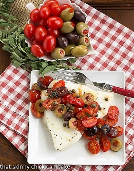 Sea Bass with Tomatoes, Olives and Capers on white plate viewed from above.