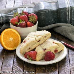 2 strawberry scones on a white plate next to half an orange and a bowl of berries