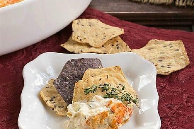 Hot Artichoke Shrimp Dip on a square white plate with chips and a sprig of thyme