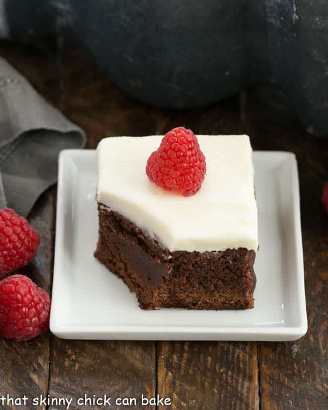A frosted raspberry brownie on a square white plate with a bite removed.