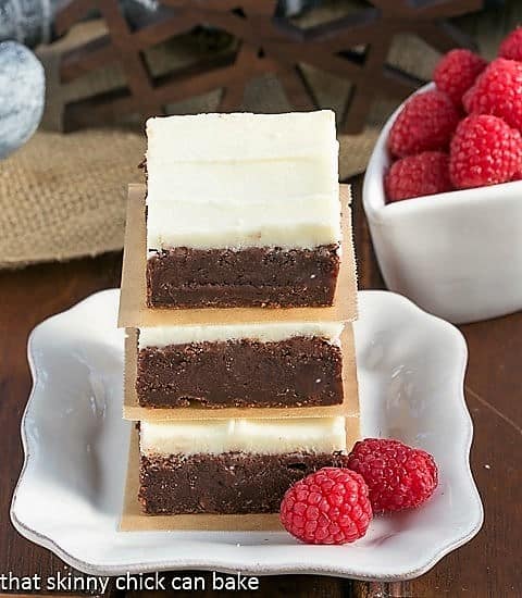 Raspberry Brownies with White Chocolate Icing on a small white plate in front of a bottle of Chambord. 