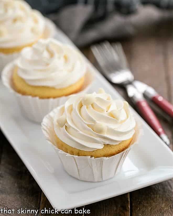 Ghirardelli Vanilla Cupcakes with White Chocolate Buttercream - tender vanilla cupcakes with a luscious swirl of Swiss meringue buttercream flavored with white chocolate! Ghirardelli Vanilla Cupcakes with White Chocolate Buttercream on a white ceramic tray