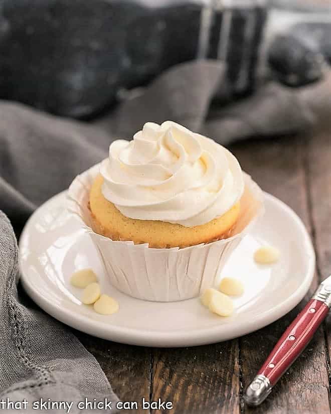 Ghirardelli Vanilla Cupcakes with White Chocolate Buttercream on a round white plate with white chocolate chips.