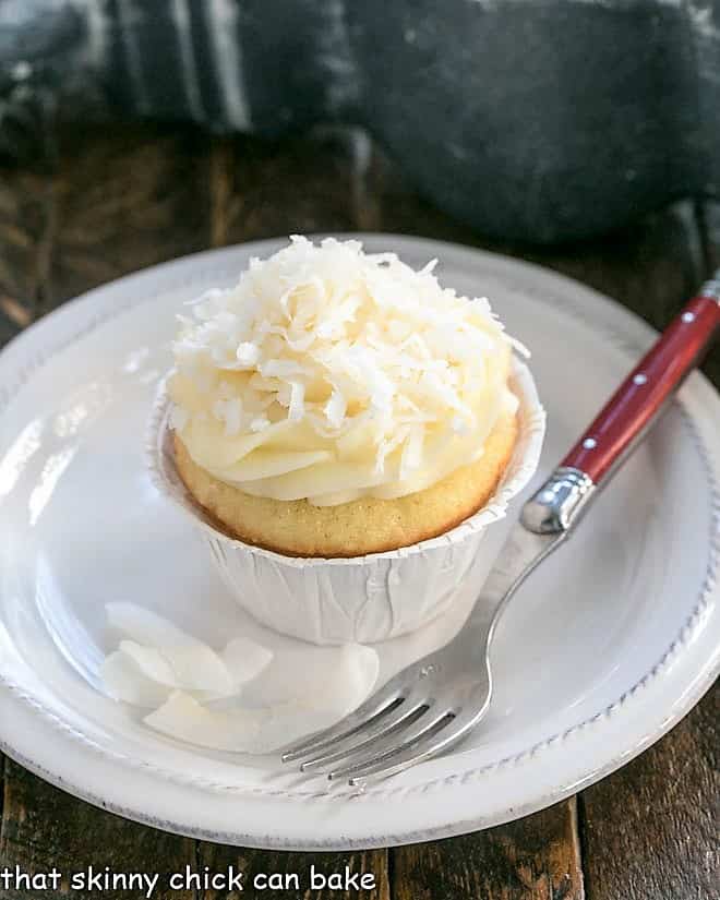 Coconut Cupcakes with Cream Cheese Frosting - Sweet, tender coconut dessert with a luscious mound of frosting! Coconut Cupcakes with Cream Cheese Frosting on a small white plate.