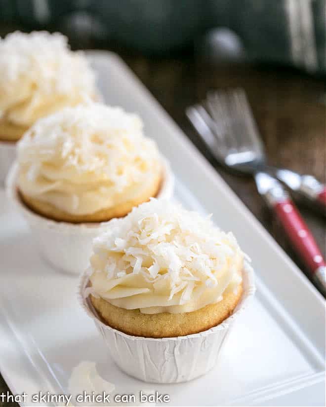 Coconut Cupcakes with Cream Cheese Frosting - Sweet, tender coconut cupcakes with a luscious mound of frosting! Coconut cupcakes on a white tray.