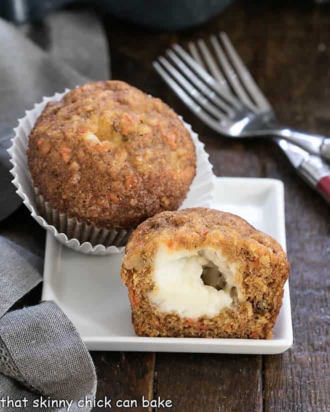 A carrot cake muffin cut in half to reveal the cream cheese center on a square white plate