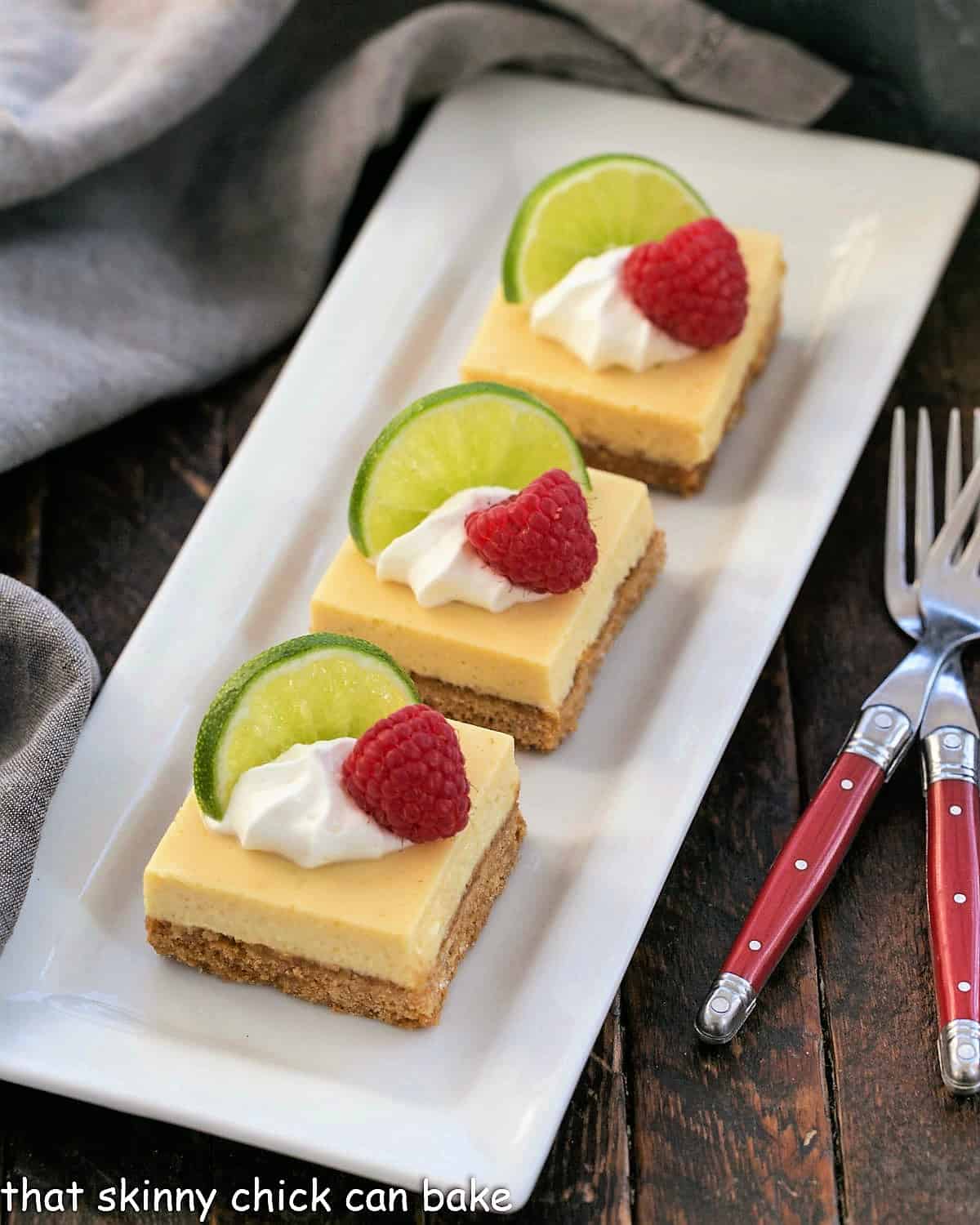 3 key lime pie bars garnished with whipped cream, lime slices and fresh raspberries.