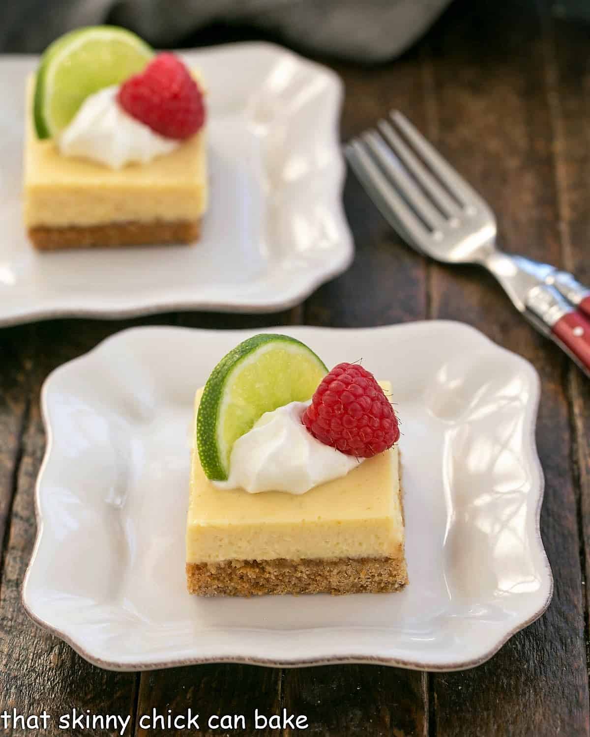 2 key lime pie bars on white plates with red handle forks.