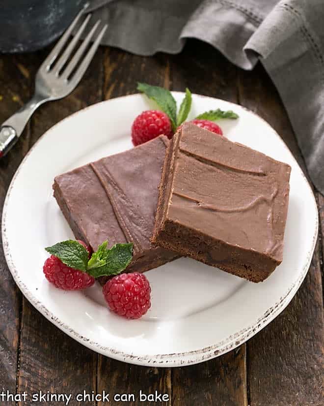 Overhead view of 2 chocolate poke cake brownies on a round white dessert plate.