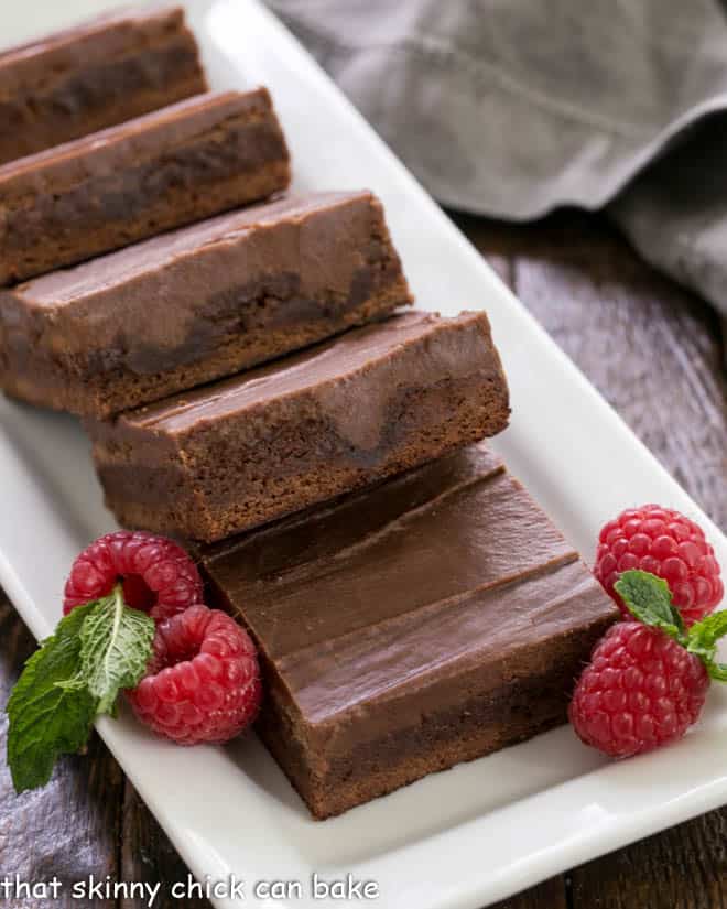 Close up of poke brownies on a white tray with fresh raspberry garnish.