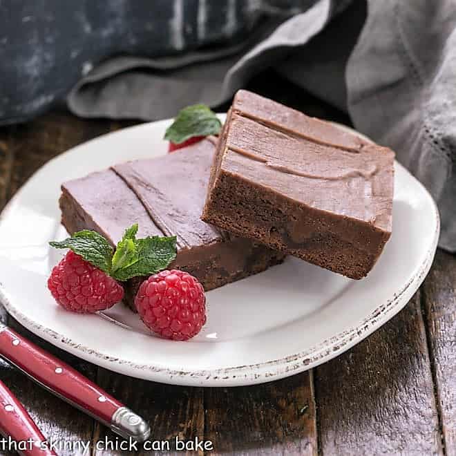 2 poke cake brownies on a round white plate with raspberries and a mint garnish