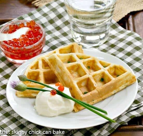 Smoked Salmon Waffles on a white plate with creme fraiche, salmon roe and chive blossoms.