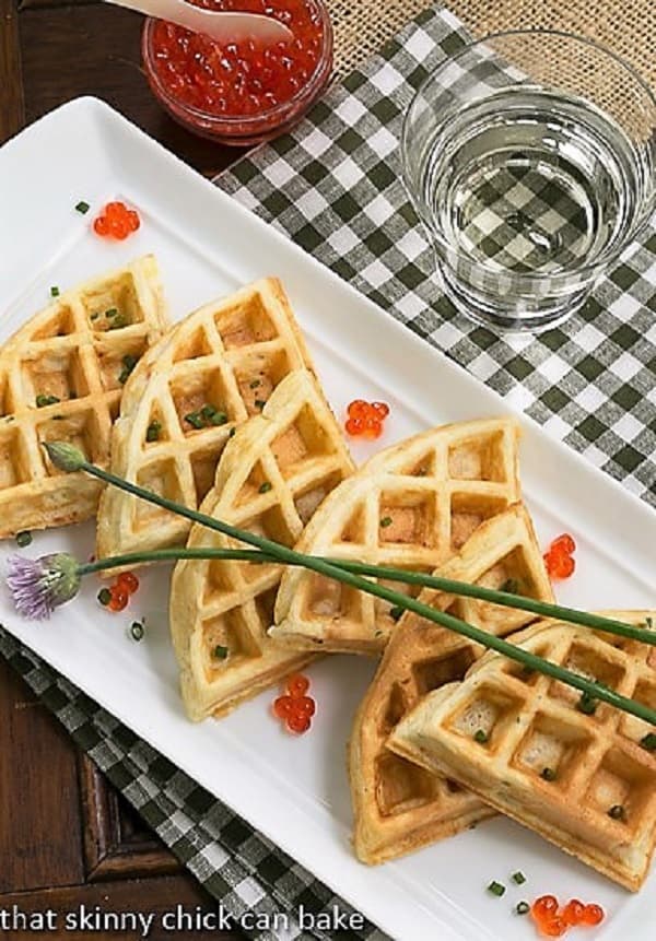 Smoked Salmon Waffles lined up on a white serving tray with chive blossoms and salmon roe