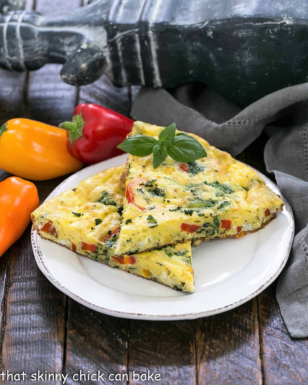 2 slices of egg frittata on a white plate with mini peppers in the background.