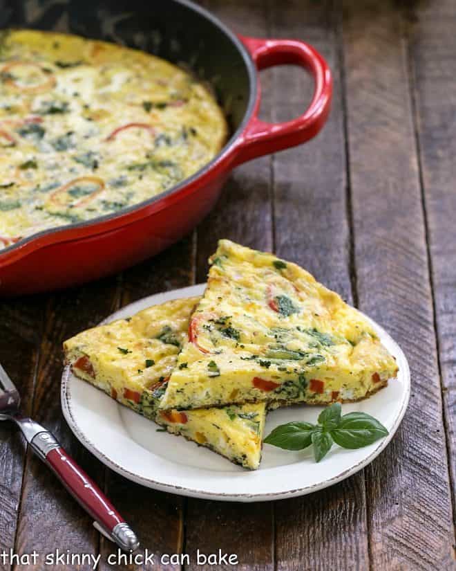 Two slices of breakfast frittata on a white plate in front of a cast iron skillet