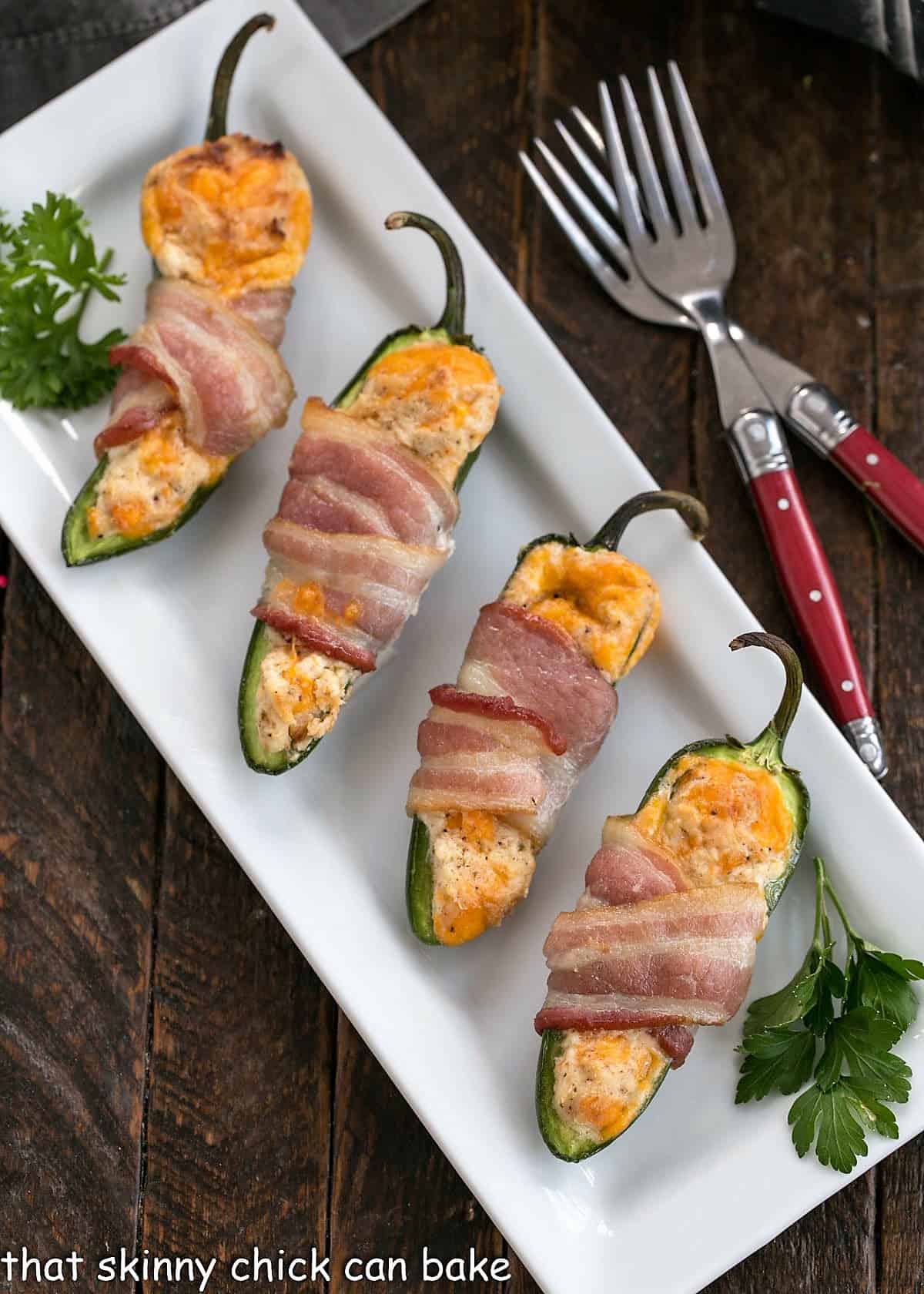 Overhead view of 4 jalapeno poppers on a white tray with 2 red handled forks.