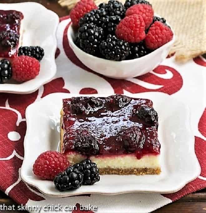 Berry Topped Cheesecake Bars sliced and served on white plates with berries