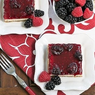 Overhead view of blackberry cheesecake bars on square white plates