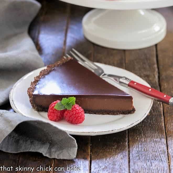 Slice of chocolate tart on a round white plate with a red fork