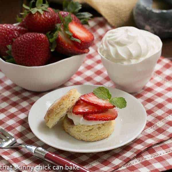 Double strawberry rose shortcake on a white plate next to bowls of strawberries and cream