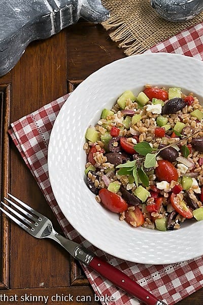 Overhead view of Greek Farro Salad in a white bowl on a red and white checked napkin.