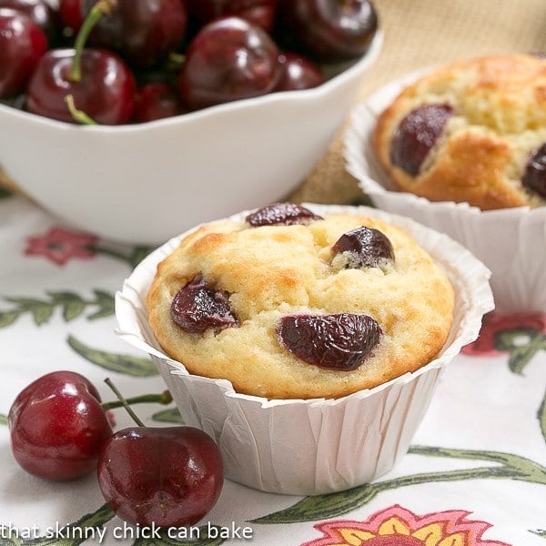 Double Cherry Muffins close up view with fresh cherries in a white bowl on a floral napkin