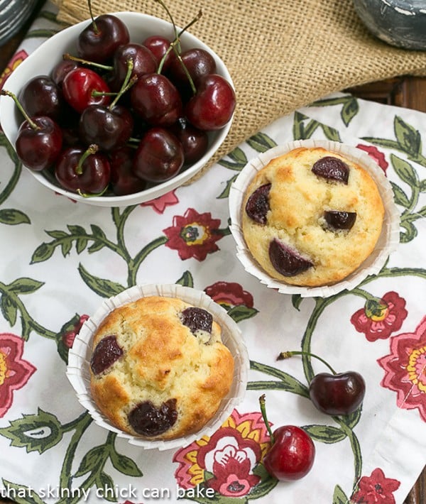 Double Cherry Muffins on a floral napkin with a bowl of dark cherries in a white bowl