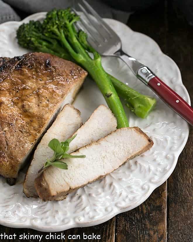 A partially sliced pork chop on a white plate with baby broccoli spears.