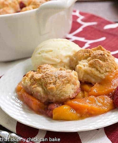 Peach Raspberry Cobbler on a white dessert plate with a scoop of vanilla ice cream.